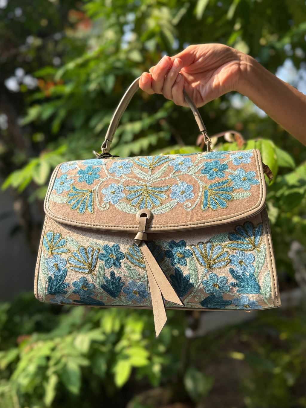 Handbag with floral pattern held by a hand against a green leafy background