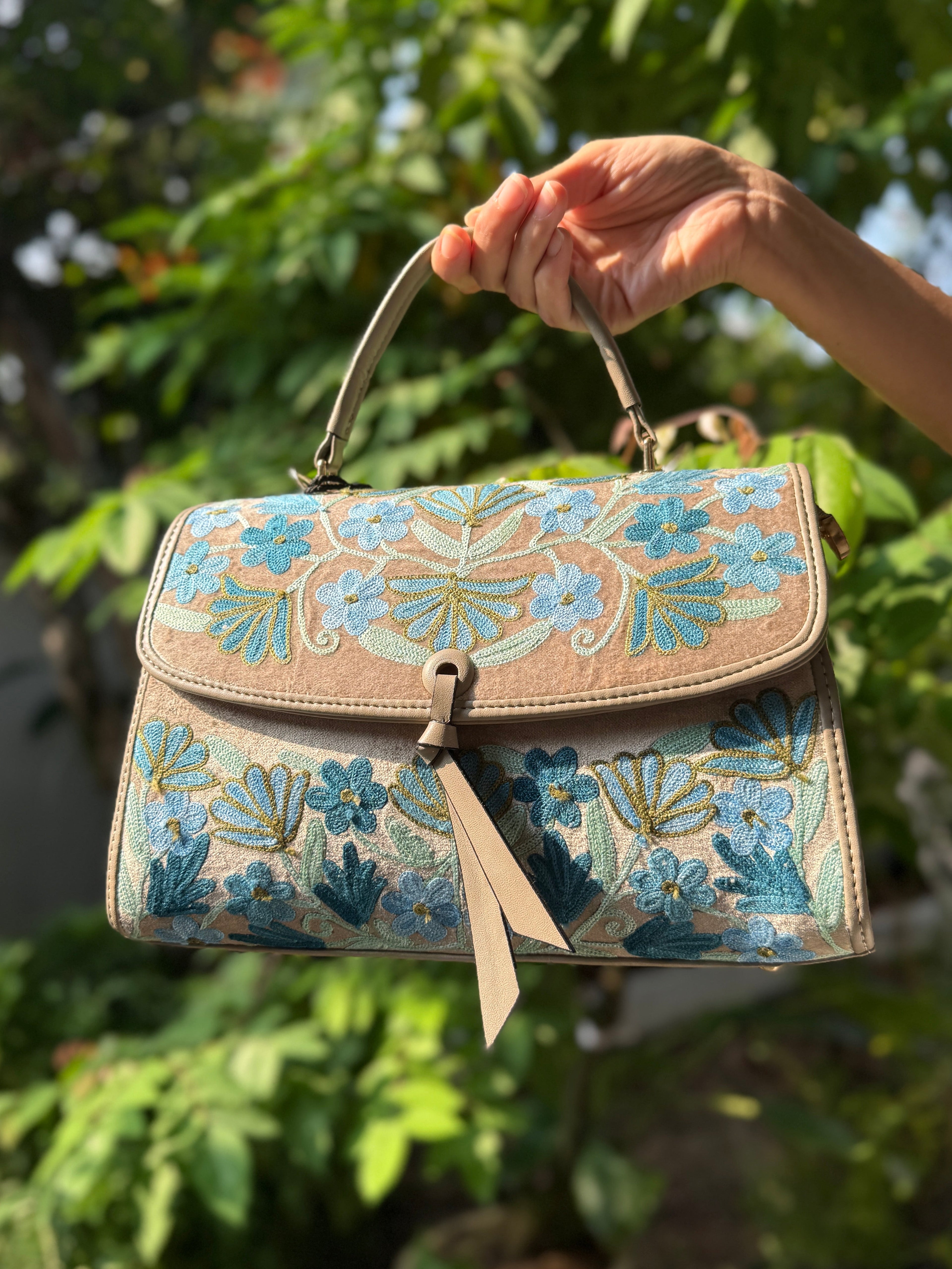 Handbag with floral pattern held by a hand against a green leafy background